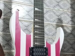 An electric guitar hanging on a wall. The guitar body is decorated with a design inspired by the American flag, featuring red and white vertical stripes on the upper part and a blue field with white stars on the lower part. The guitar has two humbucker pickups, one single-coil pickup, and a black fretboard with white triangular inlays.