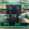 A UHF professional wireless microphone system model EA-9900 displayed on a workbench. Two handheld wireless microphones are standing on top of the receiver unit. The receiver's digital display is illuminated in green, showing channel frequencies (664.750 MHz and 689.750 MHz), signal strength, and volume levels. The setting appears to be a manufacturing or testing facility with a keyboard, monitor, and various equipment in the background.