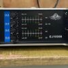 A silver and black Ejimek Japan EJ10000 audio amplifier resting on a worn wooden surface. The front panel displays four blue channel volume knobs labeled Ch.A, Ch.B, Ch.C, and Ch.D, alongside LED signal meters and clip indicators. The amplifier has ventilation slots on both sides.