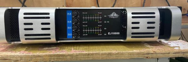 A silver and black Ejimek Japan EJ10000 audio amplifier resting on a worn wooden surface. The front panel displays four blue channel volume knobs labeled Ch.A, Ch.B, Ch.C, and Ch.D, alongside LED signal meters and clip indicators. The amplifier has ventilation slots on both sides.