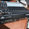 Ejimek Japan PHY-12D USB professional audio mixer placed on a wooden table. The mixer has multiple sliders, knobs, input ports, and control buttons. The device is black with white and colored controls, labeled “PROFESSIONAL AUDIO MIXER” on the side.
