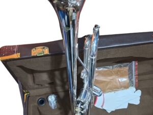 A shiny silver trumpet placed inside a brown cushioned case. The case also contains a mouthpiece, a pair of white gloves, a cleaning cloth in a plastic bag, and a small bottle of valve oil.