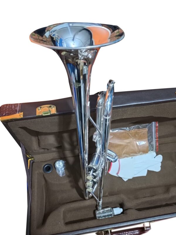 A shiny silver trumpet placed inside a brown cushioned case. The case also contains a mouthpiece, a pair of white gloves, a cleaning cloth in a plastic bag, and a small bottle of valve oil.