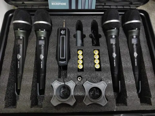A professional wireless microphone kit featuring four black DN-W1500PRO UHF handheld microphones, a single wireless receiver with a 6.35mm plug, eight AA batteries, two anti-roll mic holders, a USB charging cable, and an instruction manual, all organized in a foam-lined black carrying case.