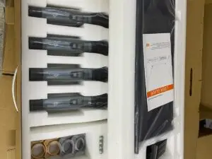 A boxed set containing four handheld UHF wireless microphones neatly arranged in foam padding. The package also includes a user guide, wireless receiver, power adapter, color-coded mic holders (gray and gold), and four AA batteries. The set appears ready for shipment or display in a factory or warehouse setting.