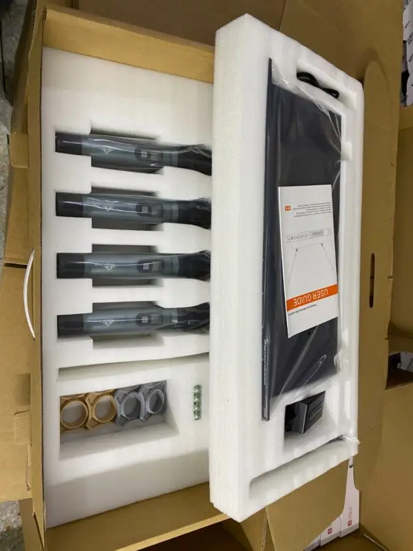 A boxed set containing four handheld UHF wireless microphones neatly arranged in foam padding. The package also includes a user guide, wireless receiver, power adapter, color-coded mic holders (gray and gold), and four AA batteries. The set appears ready for shipment or display in a factory or warehouse setting.